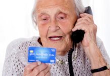 telefoniczni oszuści - siwowłosa staruszka, podaje przez telefon dane ze swojej karty kredytowej, którą trzyma przed sobą.