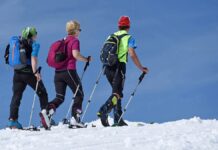 trasy narciarskie - trzech narciarzy w kolorowych strojach uprawia skitour. Idą po białym śniegu na tle błękitnego nieba.