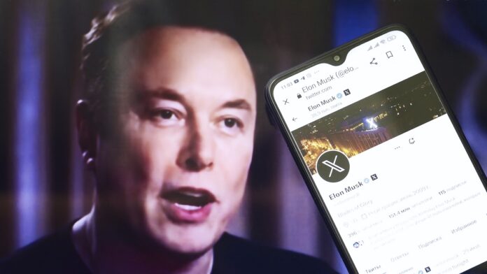 Elon Musk - zbliżenie na ekran smartfona z wyświetlonym profilem Elona Muska. W tle lekko rozmyty portret Elona.