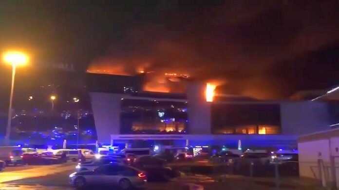 Masakra pod Moskwą - nocny widok płonącej hali koncertowej od strony parkingu pełnego samochodów.
