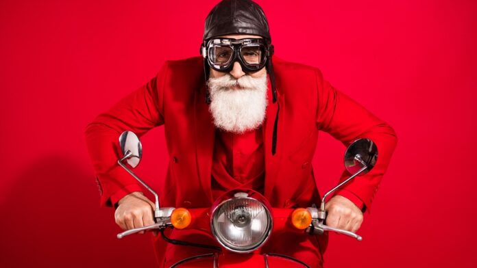 Nowelizacja unijnego prawa jazdy - wyluzowany Święty Mikołaj ubrany w czerwony garnitur, ma na głowie skórzaną pilotkę i gogle. Jedzie na czerwonym skuterze, ma poważną twarz i długą białą brodę. Czerwone tło.