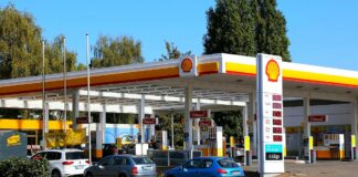 Wielomilionowa kara grozi Shell Polska - widok stacji paliw w barwach Shella. Biała z żółto-czerwonymi akcentami. Do dystrybutorów stoi kolejka samochodów, w oddali firmowy sklep.