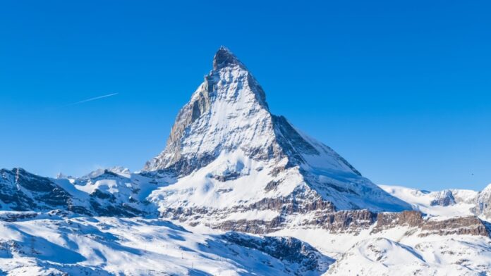 Tragedia w Alpach - widok na ogromną, ośnieżoną górę w Alpach. Skalisty, pokryty śniegiem szczyt na tle bezchmurnego, błękitnego nieba.