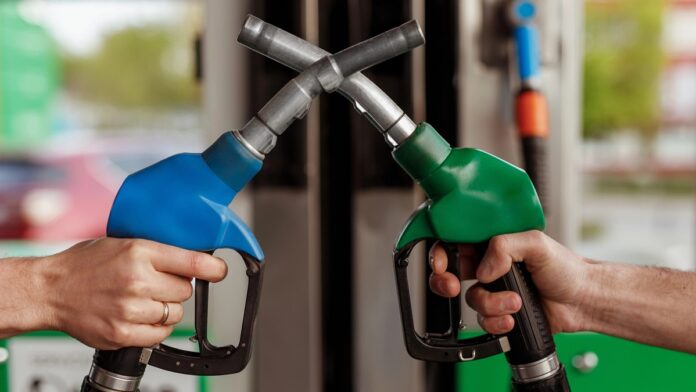 biopaliwo 100% - dwie ręce trzymają skrzyżowane ze sobą pistolety nalewaków paliwa. Po lewej niebieski, po prawej zielony.