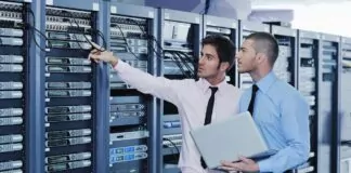 centra danych - dwaj młodzi inżynierowie w białych koszulach znajdują się w serwerowni w otoczeniu licznych szaf komputerowych.