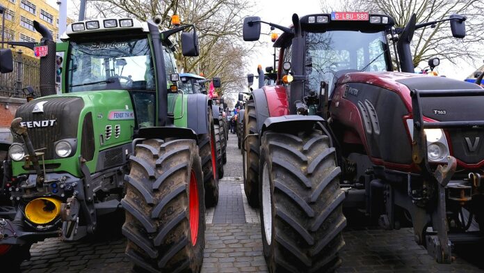 fala rolniczych protestów - podwójny rząd ogromnych maszyn rolniczych blokujących drogę.