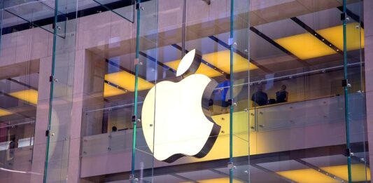 Firma Apple - Na przezroczystej, szklanej elewacji domu towarowego widać ogromne, biało-podświetlone logo firmy. Ugryzione jabłko. alphabet oraz apple i meta na celowniku KE