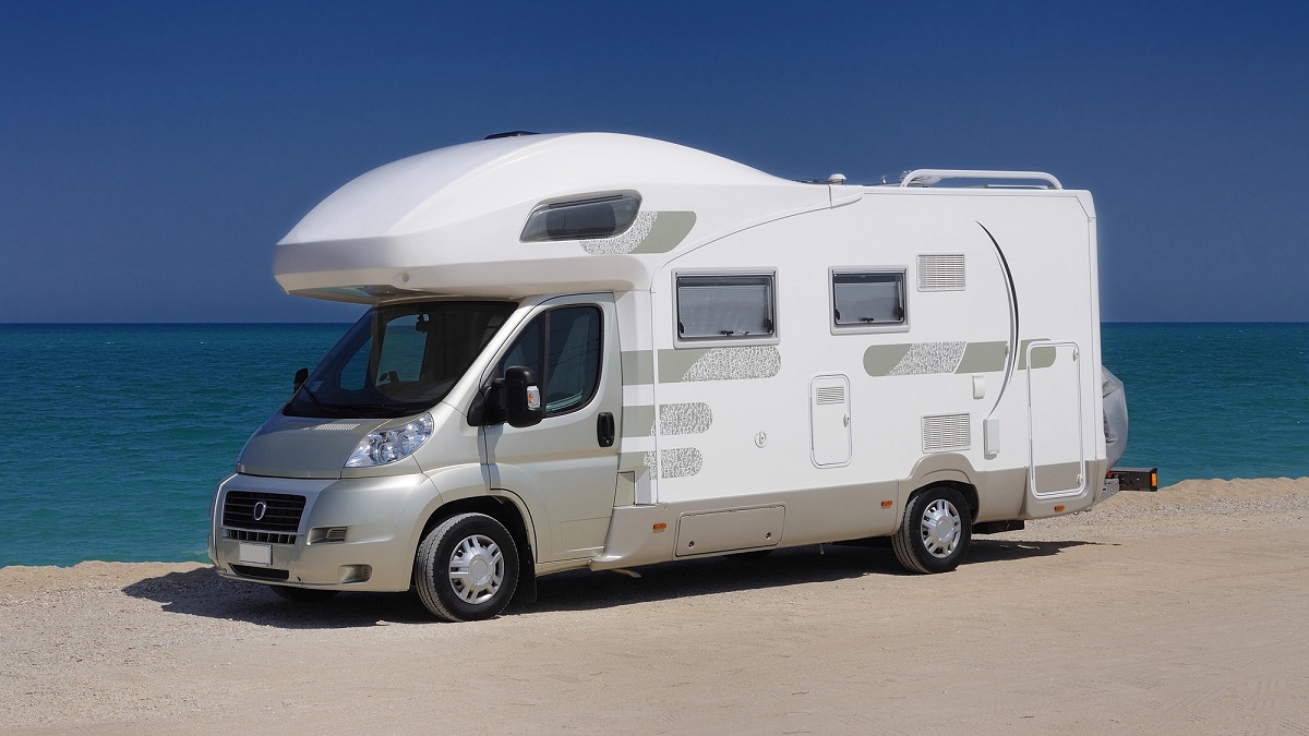 nowelizacja unijnego prawa jazdy - na piaszczystej plaży, w słoneczny dzień stoi biały samochód campingowy. W tle błękitne morze i bezchmurne niebo.