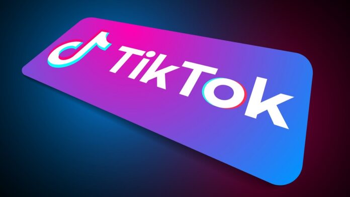 Ciąg dalszy problemów TikToka - komputerowe wyobrażenie leżącego smartfona. Na fioletowo-niebieskim ekranie znajduje się duże, białe logo TikToka.