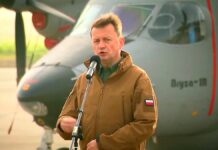 Mariusz Błaszczak - minister w wojskowej kurtce khaki, przemawia na wojskowym lotnisku, a za jego plecami stoi szary samolot Bryza.