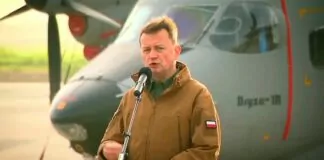 Mariusz Błaszczak - minister w wojskowej kurtce khaki, przemawia na wojskowym lotnisku, a za jego plecami stoi szary samolot Bryza.