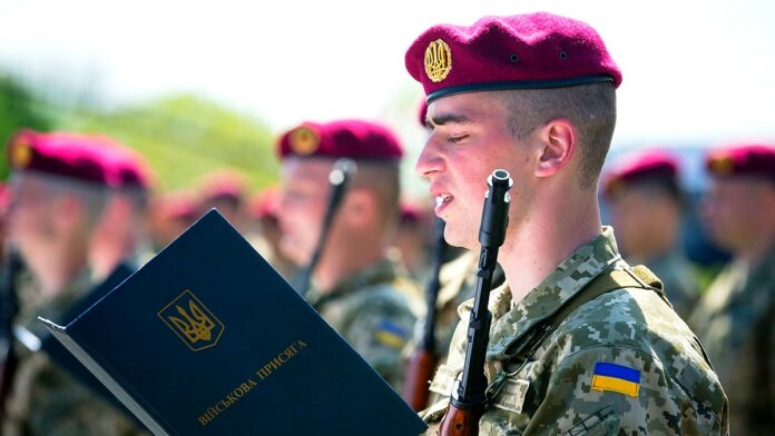 Mobilizacja w Ukrainie - grupa ukraińskich żołnierzy w mundurach polowych z czerwonymi beretami, składa przysięgę. Na piersiach przewieszone karabiny.
