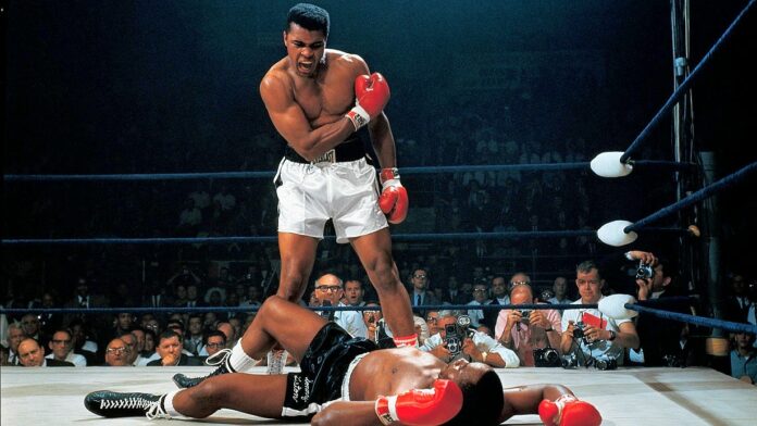 Muhammad Ali - na ringu leży czarnoskóry bokser w czarnych spodenkach, nad nim stoi czarnoskóry zwycięzca w białych spodenkach.