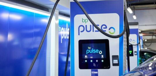 Sieć ładowania elektryków - zbliżenie na niebiesko-białą szafę, będącą ładowarką samochodów elektrycznych. Zarówno na obudowie, jak i na ekranie LCD, widoczne logo BP pulse.