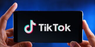 USA chcą pozbyć się TikTok-a - na niebieskim tle, dwie dłonie trzymają smartfon, na którym wyświetla się duże logo TikToka-a.