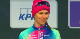 Wielki sukces Katarzyny Niewiadomej - uśmiechnięta Katarzyna stojąca na drugim miejscu podium. Ubrana w bluzę z tęczową paletą kolorów, na głowie dziana, różowa czapka.