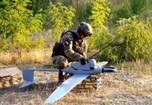 bezzałogowce flyeye - na leśnej polanie, ubrany w maskujący strój żołnierz przygotowuje do startu drona FlyEye. Dron wygląda jak duży zabawkowy model samolotu.