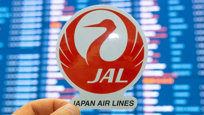 japońskie linie lotnicze - Na białym, okrągłym kartoniku znajduje się logo czyli japoński żuraw w kolorze czerwonym. Poniżej czarny napis Japan Air Lines.