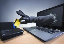 numer PESEL - z ekranu laptopa wysuwa się ręka w czarnej rękawiczce i kradnie kartę kredytową z leżącego obok portfela.