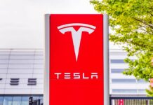 Tesla zwalnia - przed centrum serwisowym stoi pionowa, karminowo-czerwona tablica z ogromną stylizowaną literą T, w kolorze białym. Poniżej charakterystyczny, biały napis TESLA.