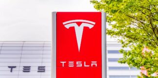Tesla zwalnia - przed centrum serwisowym stoi pionowa, karminowo-czerwona tablica z ogromną stylizowaną literą T, w kolorze białym. Poniżej charakterystyczny, biały napis TESLA.