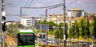 "Panorama miejska z autobusem miejskim w Poznaniu, podkreślająca rolę dofinansowania UE w rozwoju regionalnym." Premier zarabia 3x mniej