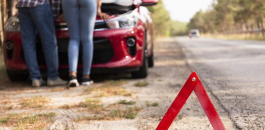 Rozładowany akumulator na trasie - trójkąt przy drodze i auto z podniesioną maską