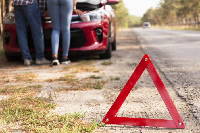 Rozładowany akumulator na trasie - trójkąt przy drodze i auto z podniesioną maską